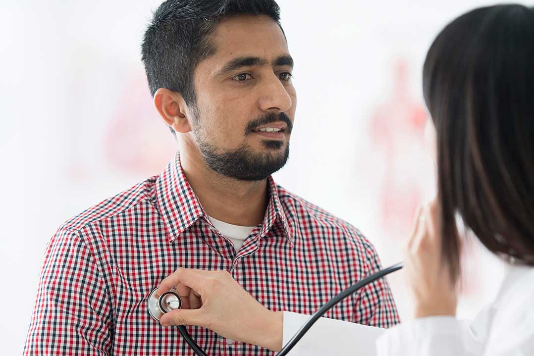 Woman checking a man’s heart rate with a stethoscope.